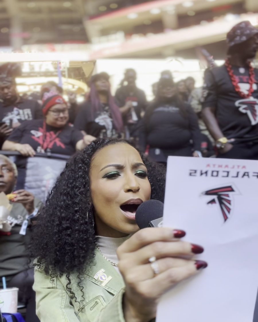 Chelsea on the mic reading a Falcons cue card in the packed stands