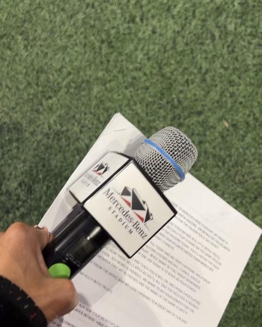 Chelsea's hand holding a mic and her script on the field