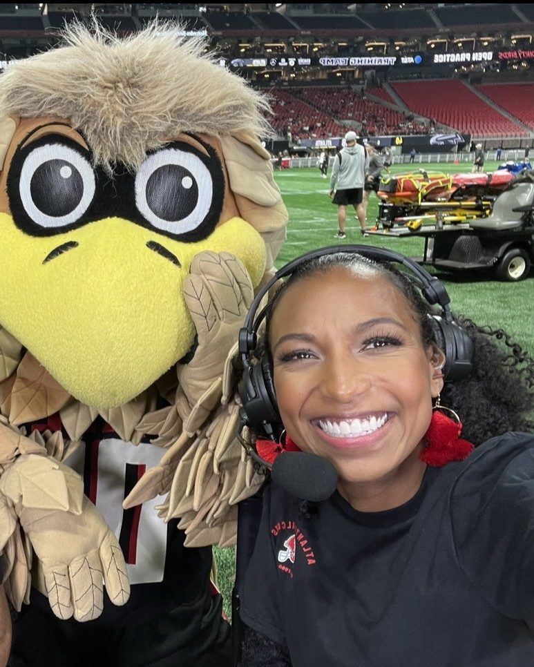 Chelsea on headset with the Falcons mascot on the field at Mercedes-Benz Stadium